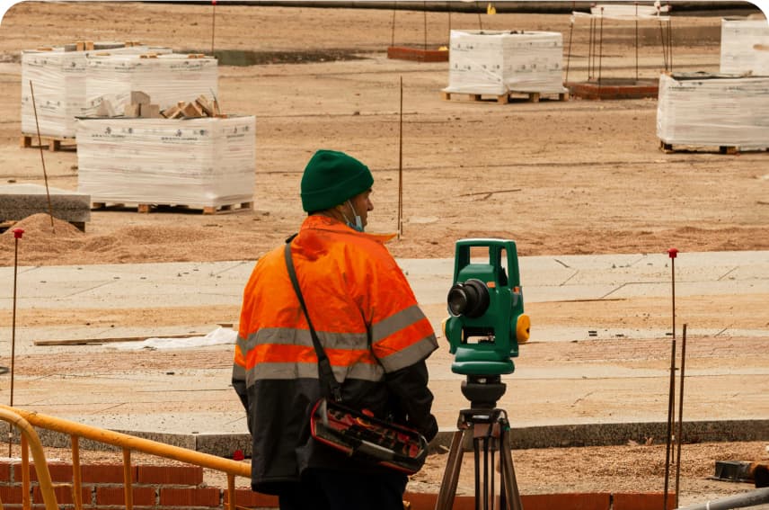 Imagen de un hombre con un teodolito en una obra en construcción midiendo volúmenes de tierra